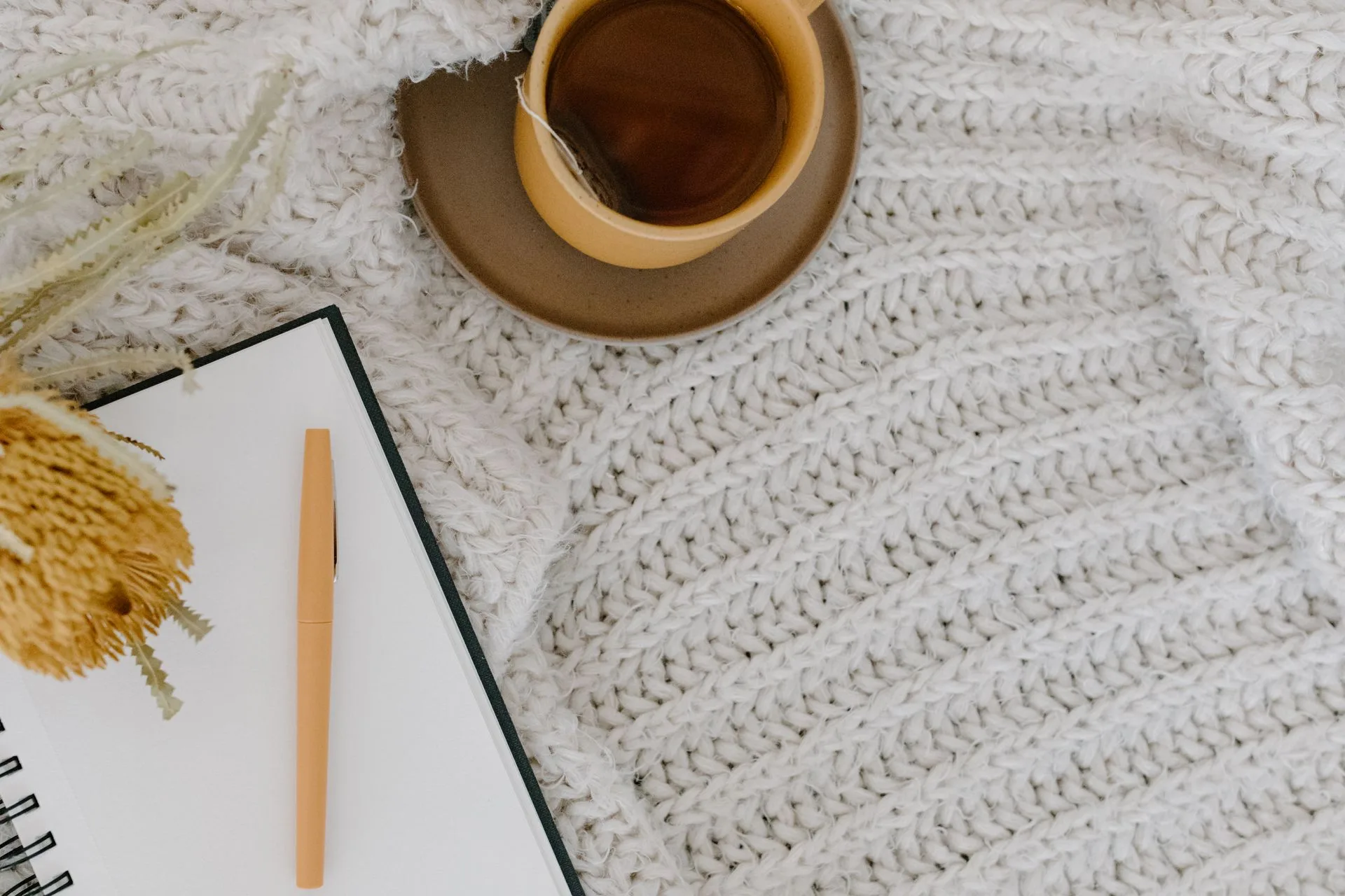 A notebook and pencil beside a cup of tea